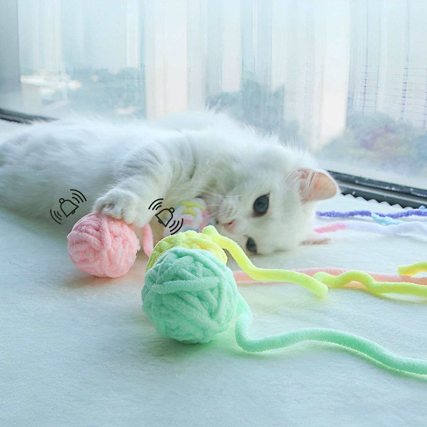 A white cat playing with three different colored yarn balls