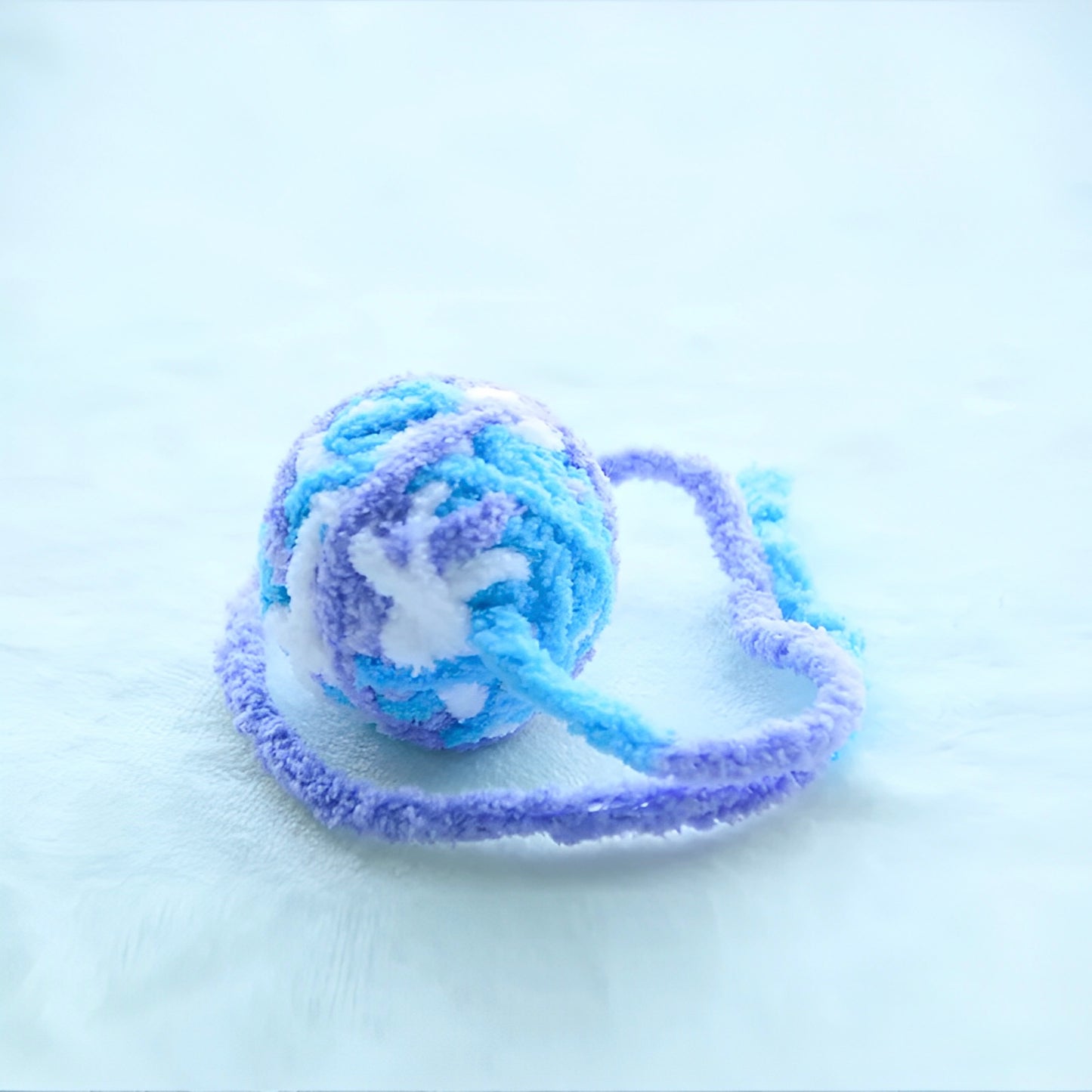 Colorful yarn balls with bells attached to a string, displayed on a white surface.