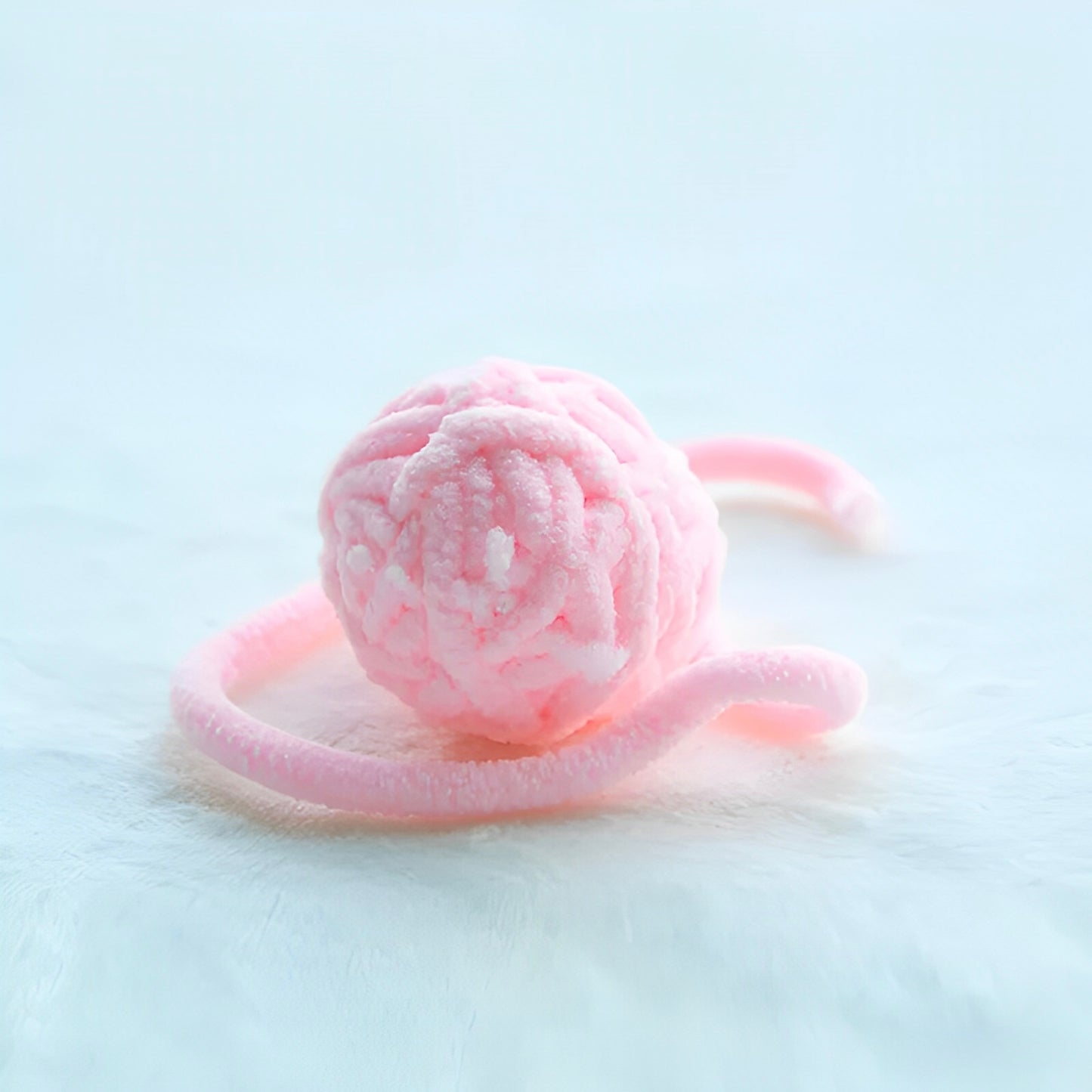 Pink yarn balls with bells attached to a string, displayed on a white surface.