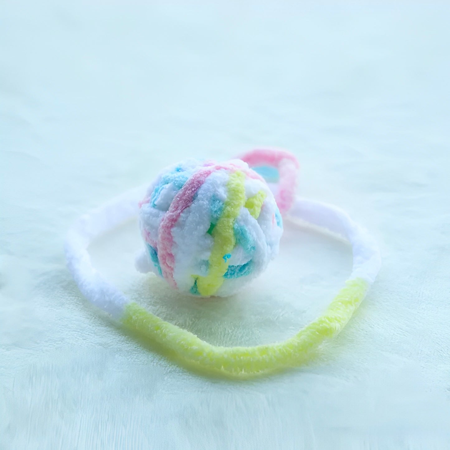 Colorful yarn balls with bells attached to a string, displayed on a white surface.