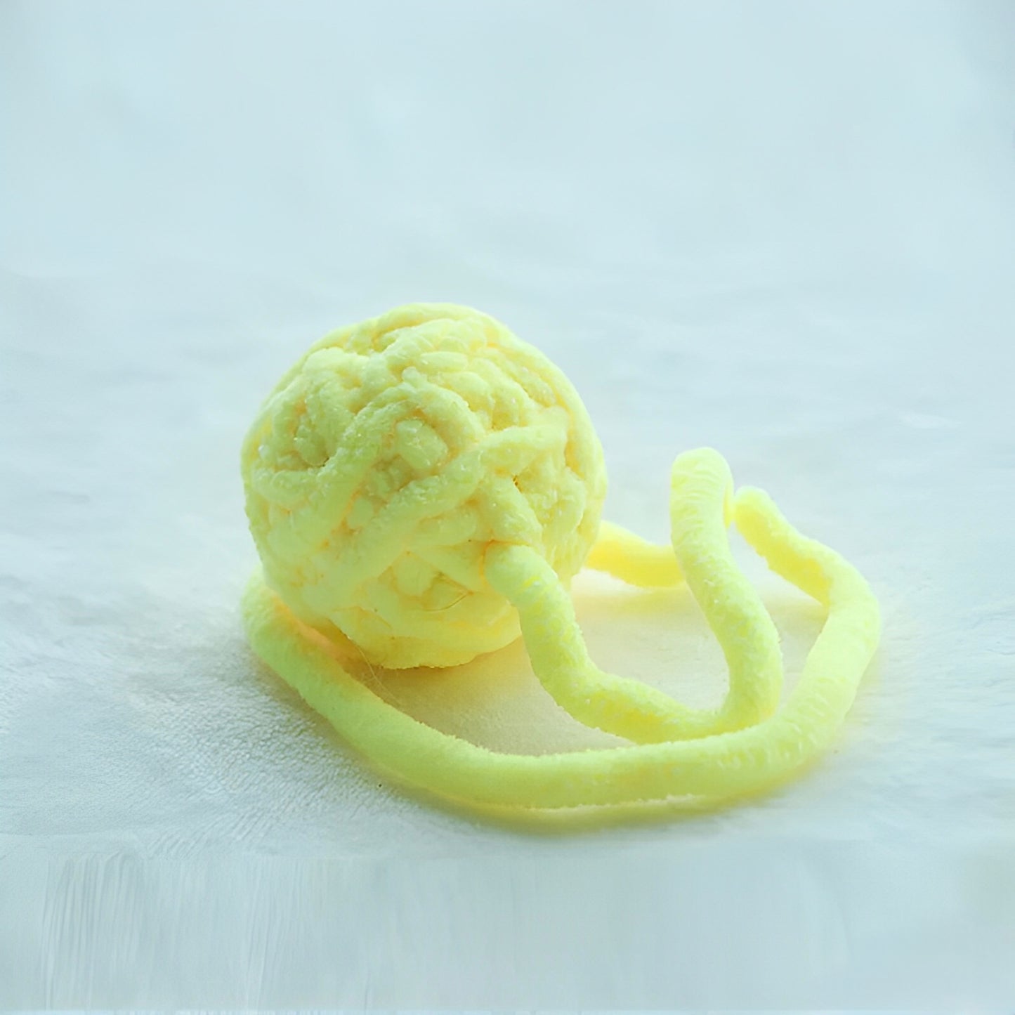 Yellow yarn balls with bells attached to a string, displayed on a white surface.