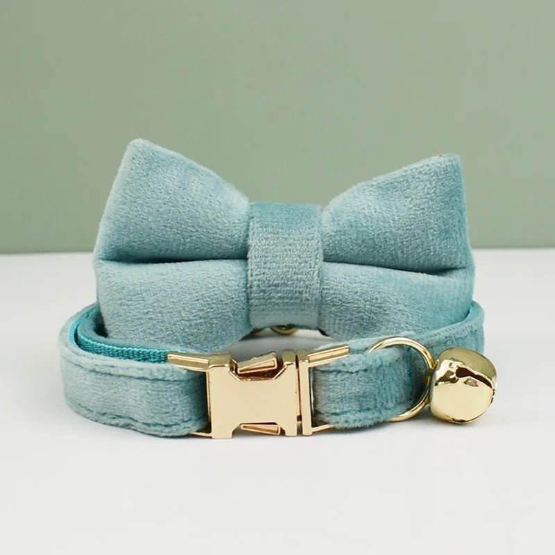 Light blue velvet bow tie and cat collar with gold clasp and bell on a light gray background