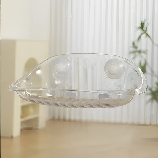 A transparent cat window bed with suction cups, placed on a glass window in front of a white wall and a potted plant.