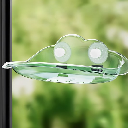 A transparent cat window bed with suction cups, placed on a glass window in front of a garden.