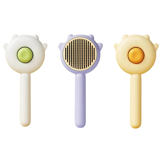 Three cat hair brushes with different colors (green, yellow, and purple) each featuring a stylized cat face at the brush head. The middle one is the purple one and shows the bristles whereas the other two, on each end, shows the back of the brush with the release button