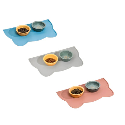 Three pet silicone mats in blue, gray, and pink with two bowls on top on a white background