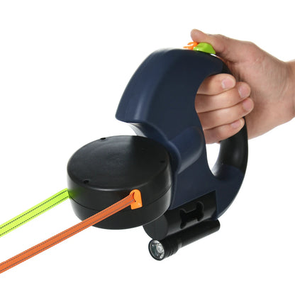 Hand holding a blue and black retractable dog leash with orange and green leashes on a white background