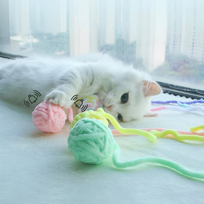 A white cat playing with three different colored yarn balls