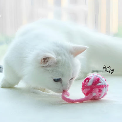 A white cat playing with a pink and white yarn ball