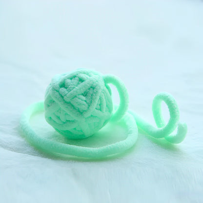 Green yarn balls with bells attached to a string, displayed on a white surface.