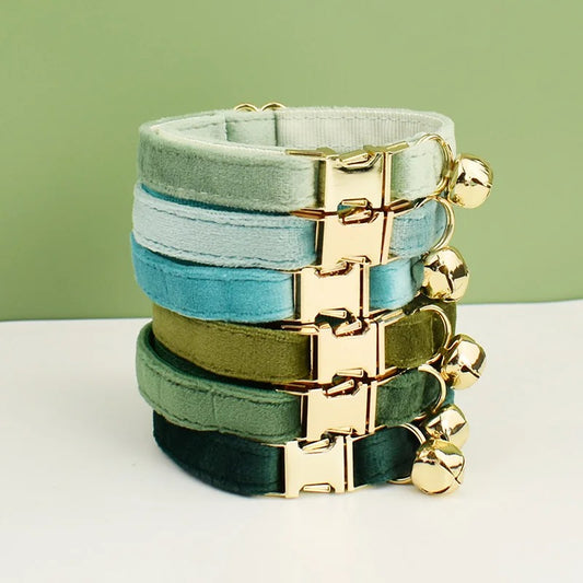 Stack of colorful cat collars with gold clasps on a white surface with a green background
