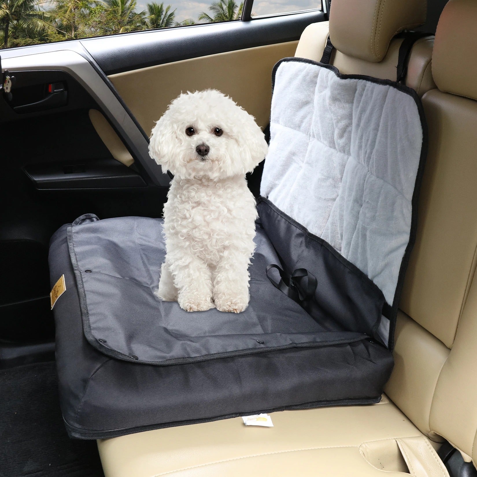 White dog sitting on a car seat cover in a vehicle